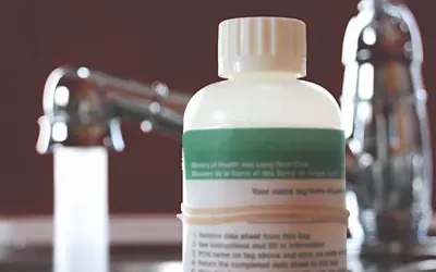 A well water sample bottle sits beside a faucet with water running